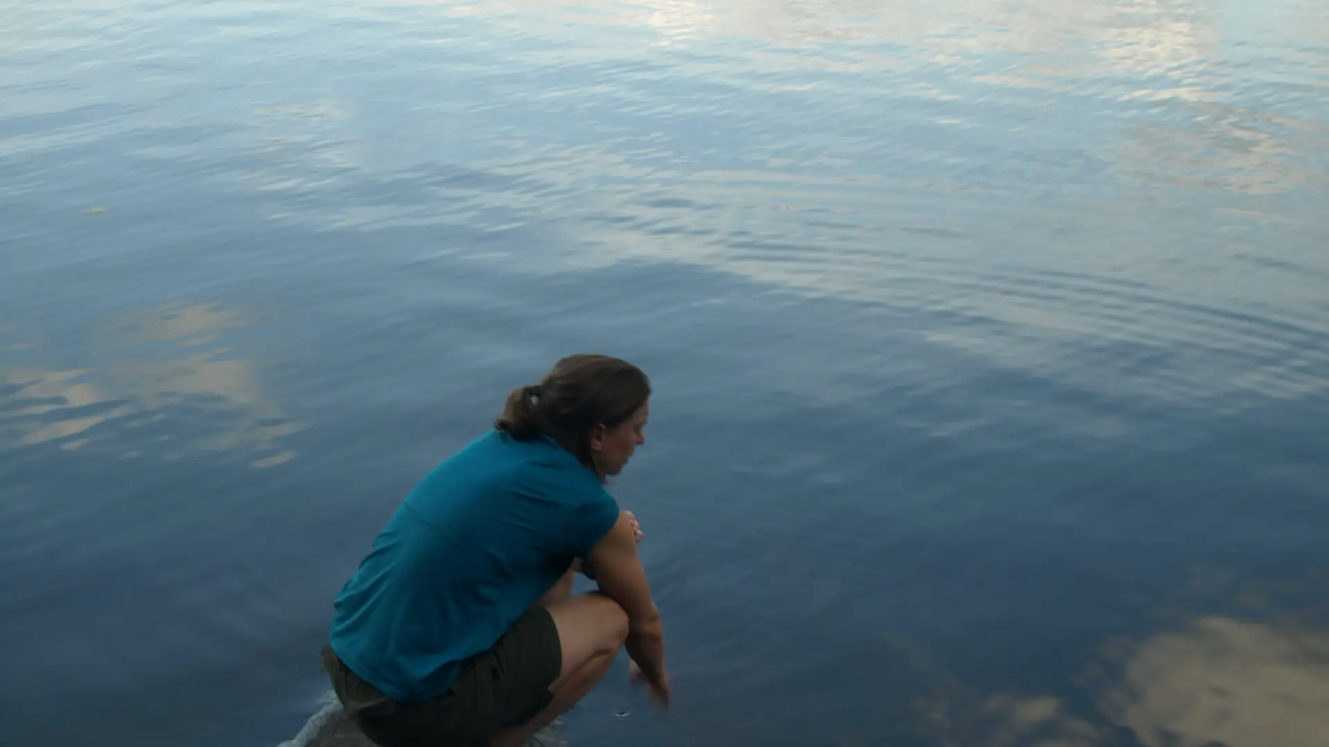 A person kneels down by the water.