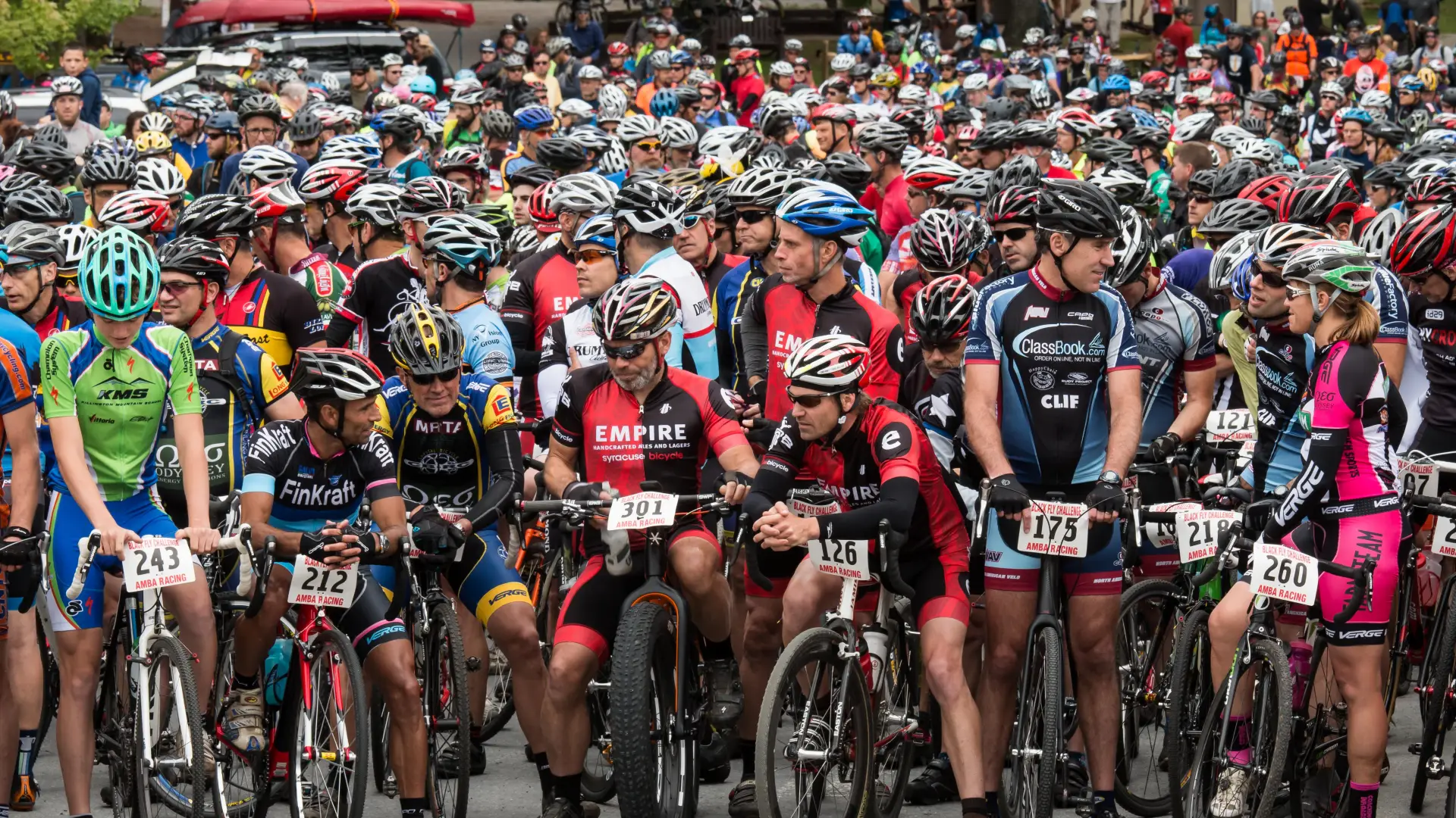 Cyclists in colorful jerseys and helmets gather at the starting line of the Black Fly Challenge in the Adirondacks.