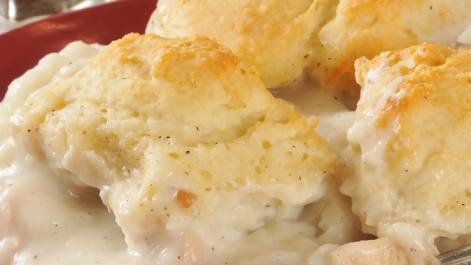 a plate full of chicken and gravy with a few biscuits on top