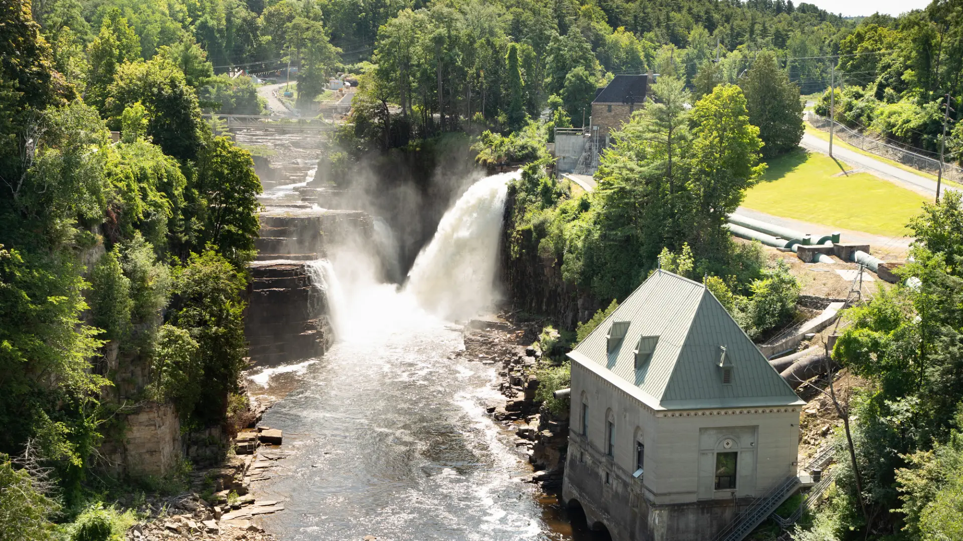 Water crashes over the falls with a building near by.