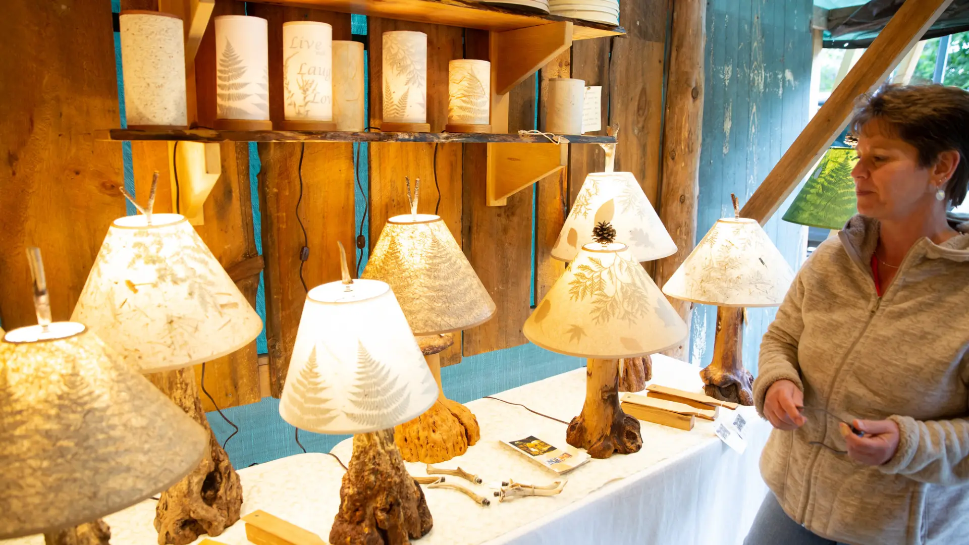 A variety of different lamps with hand made shades with fern and other rustic designs. The lamps bottoms are made of different wood or antlers