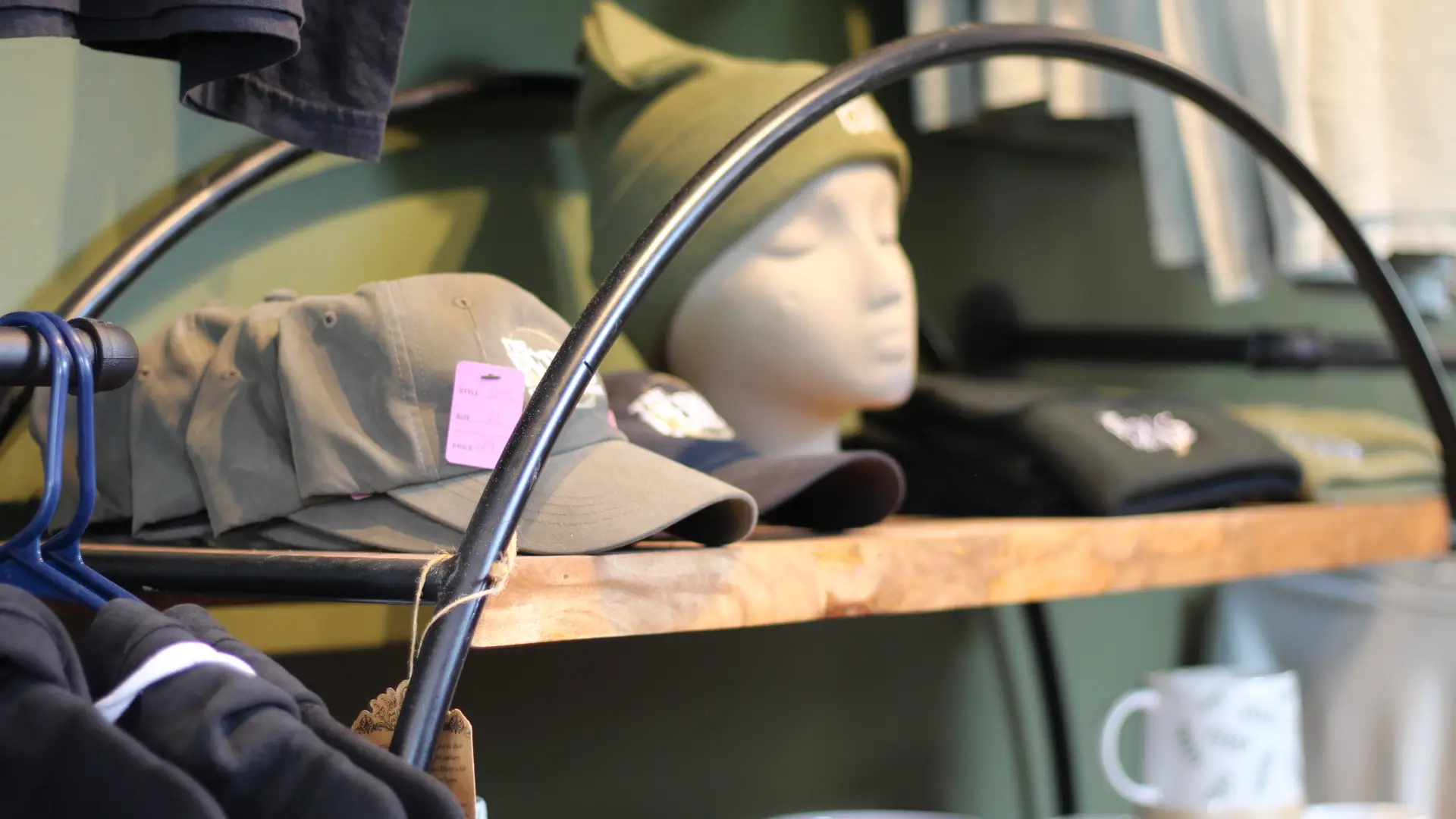 Hats adorn a mannequin head on a rough sawn shelf surrounded by other attire.
