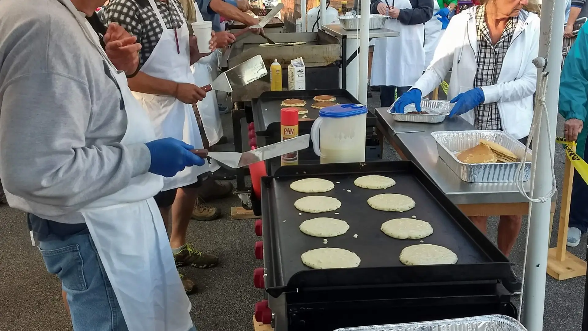 A group of volunteers cook and serve pancakes at an outdoor event.
