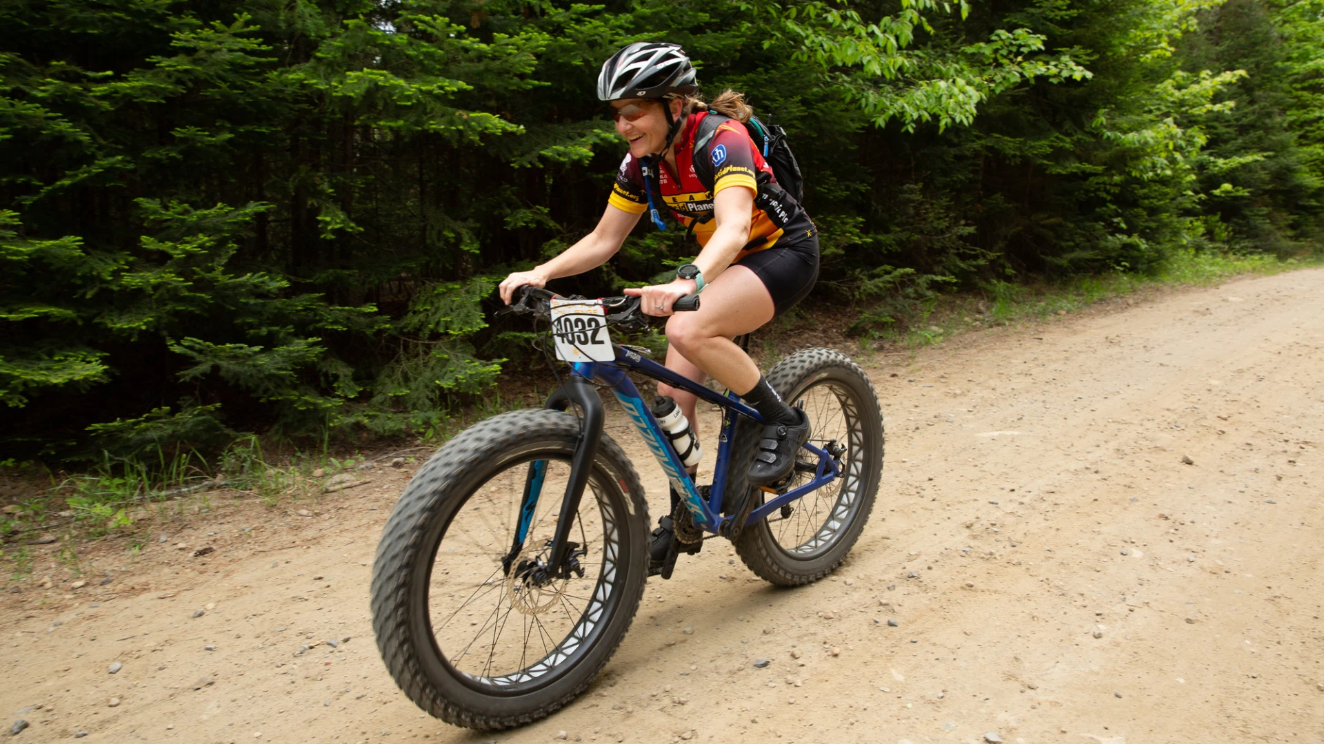 A woman in cycling gear rides a bike on a dirt trail in a forest during the Black Fly Challenge.