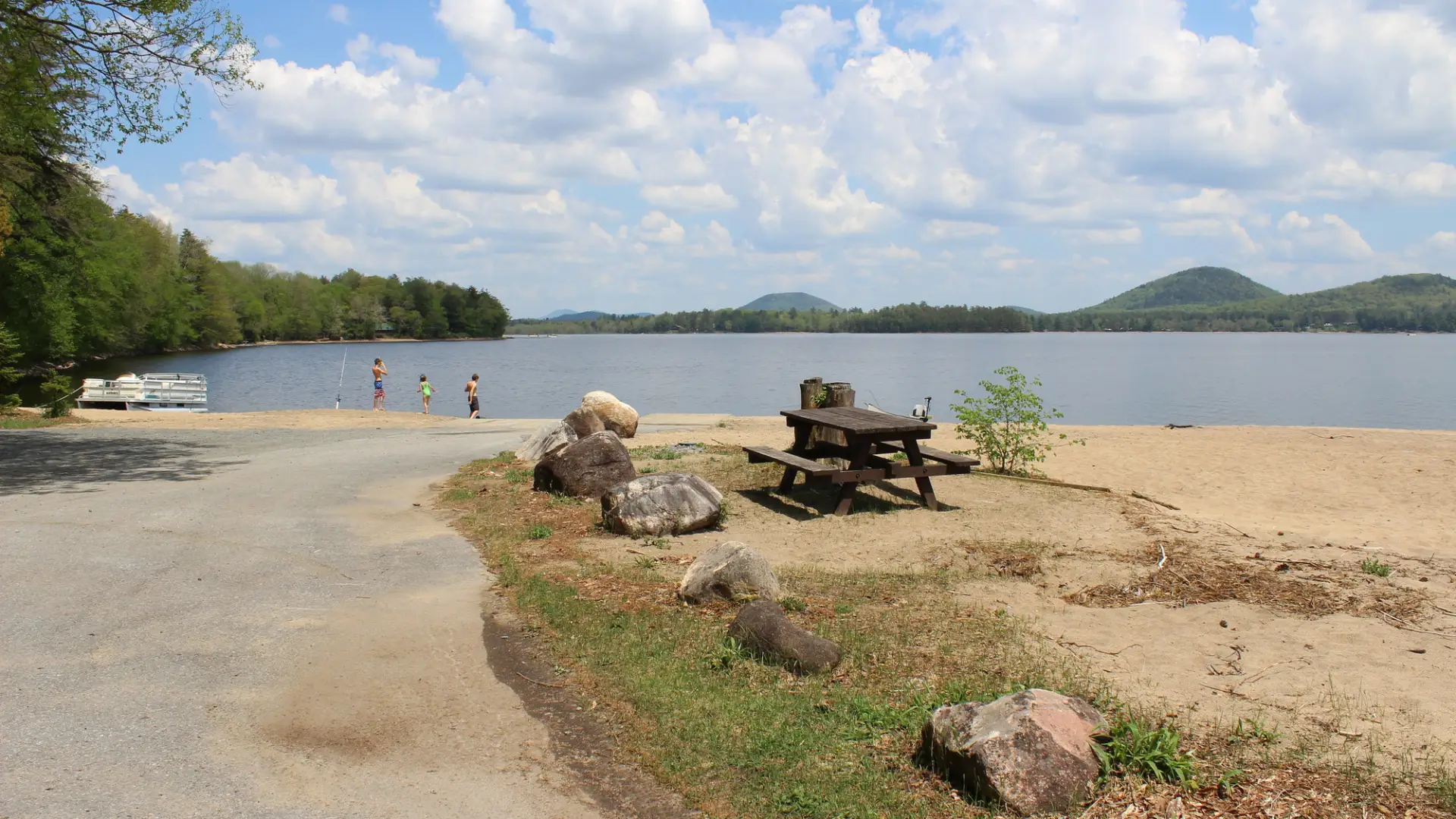A beach with a boat ramp, picnic table, and mountain views
