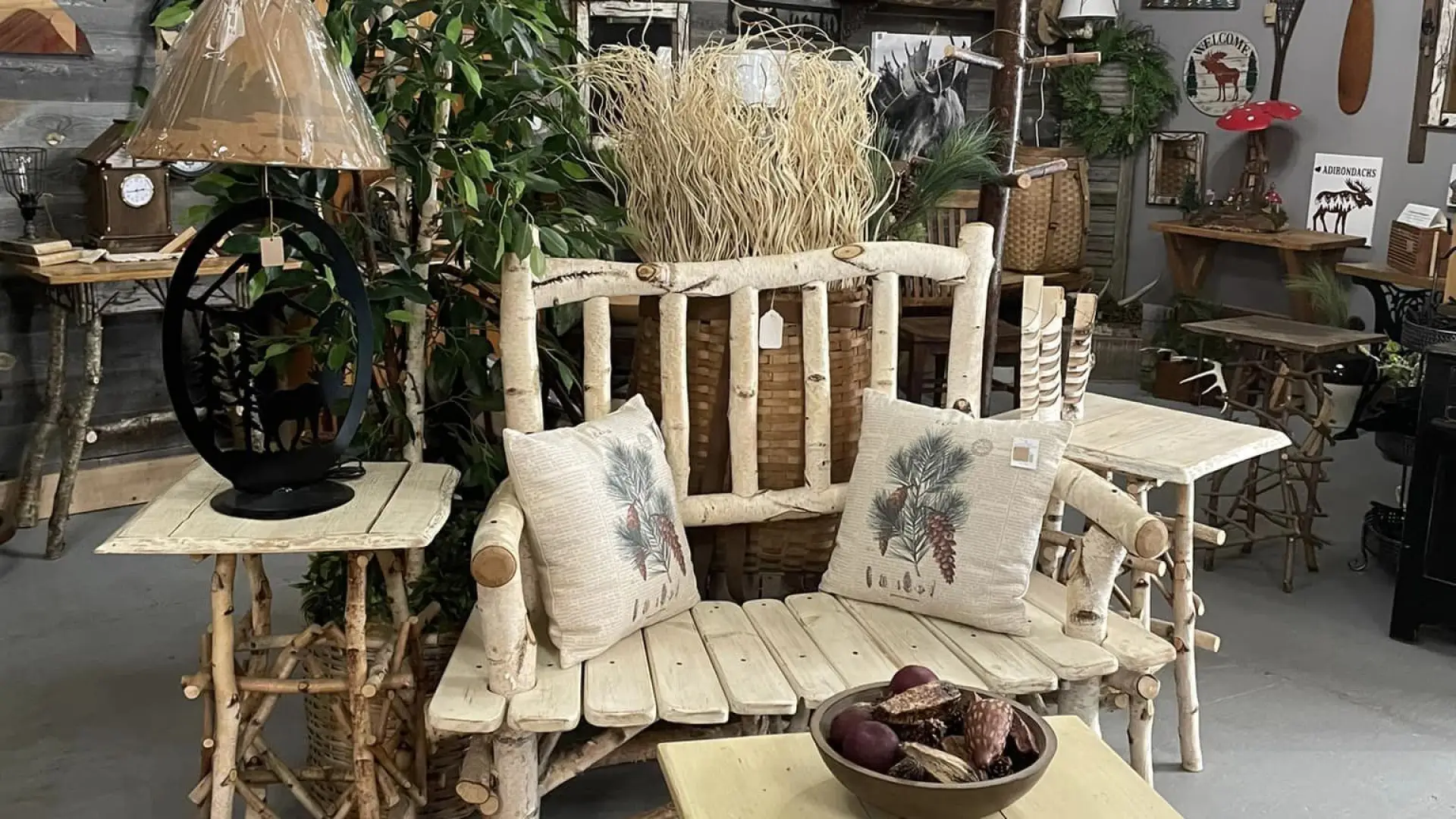 A room full of rustic decor pieces like birch wood bench and matching table and wrought iron lamps and wall hangings