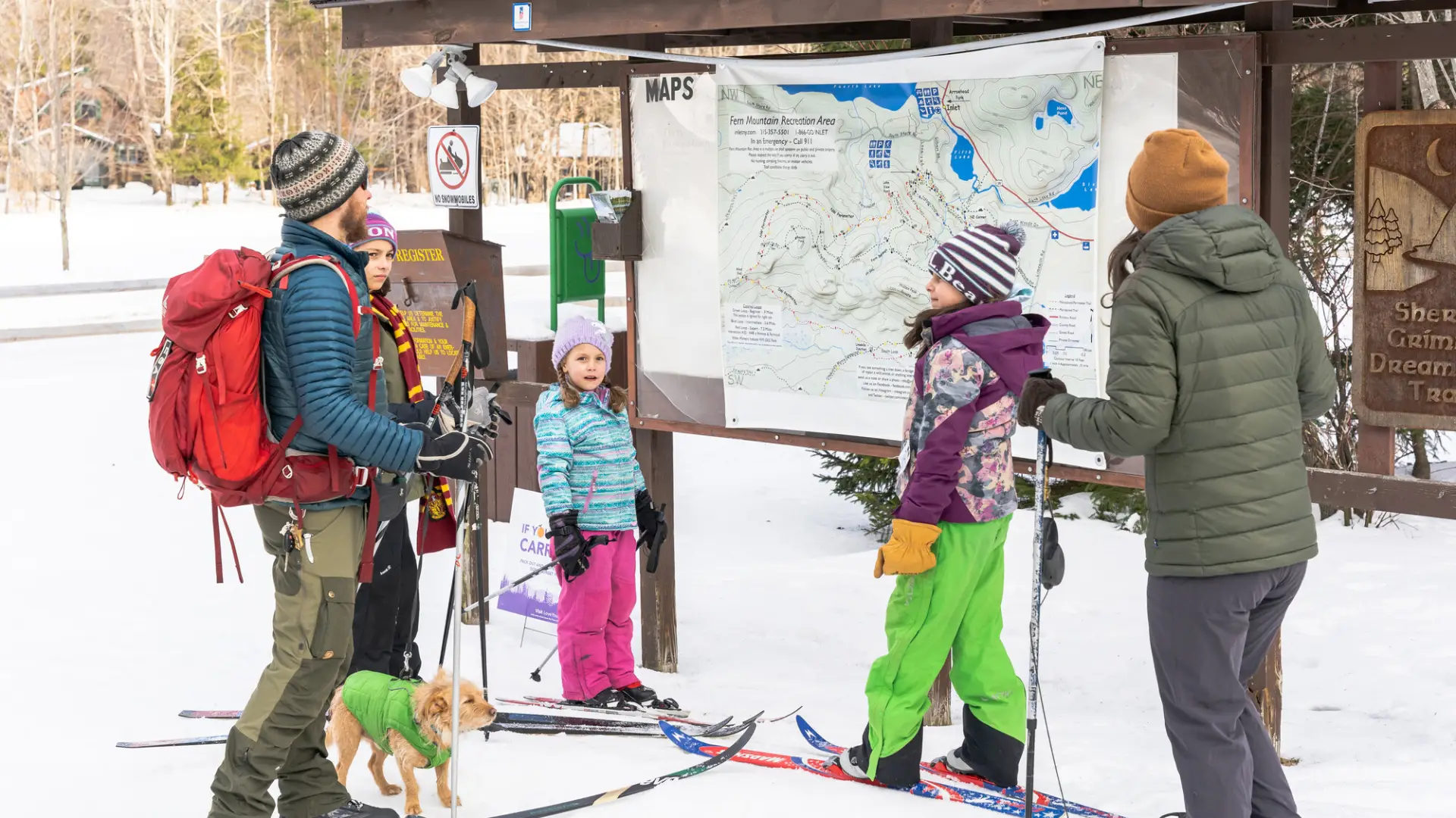 A family at a trailhead kiosk about to cross-country ski