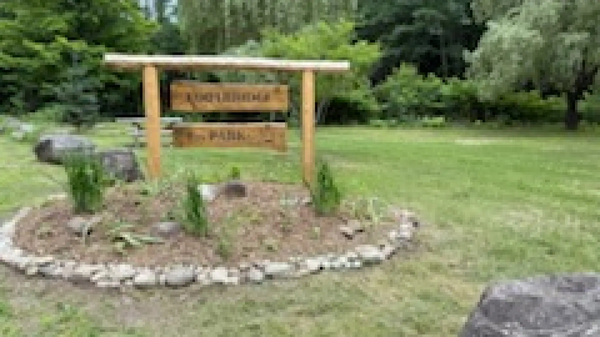 Rustic Footbridge Park sign with lawn and trees in the background