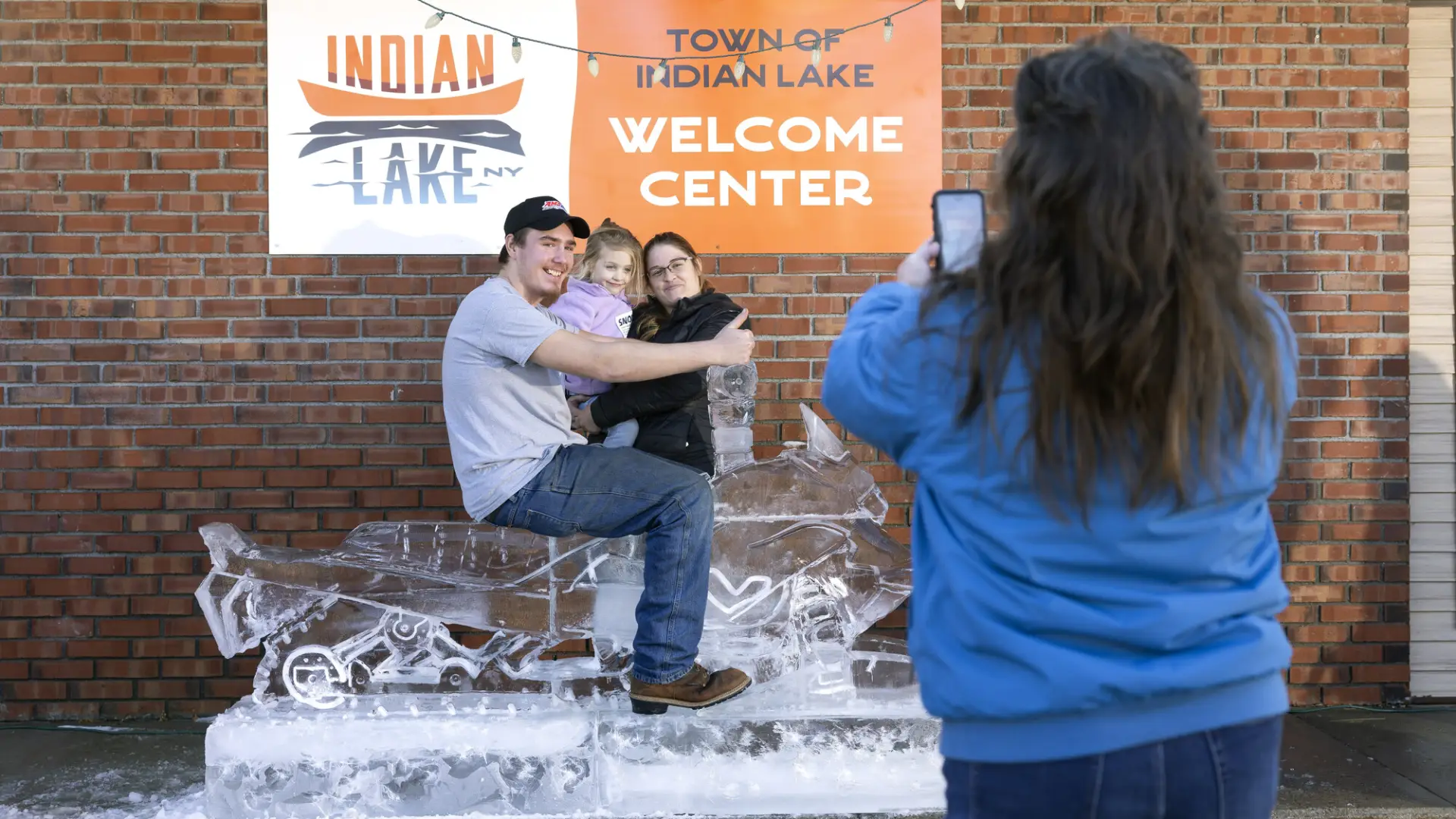 a woman taking a picture of people on the ice sculpted snowmobile