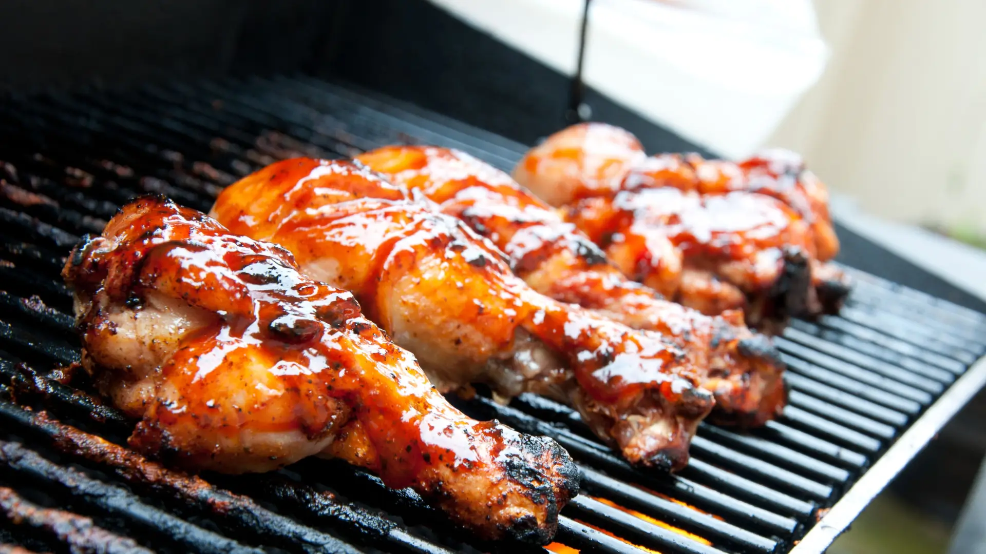 Several pieces of chicken covered in bbq sauce grilling on a black grill rack