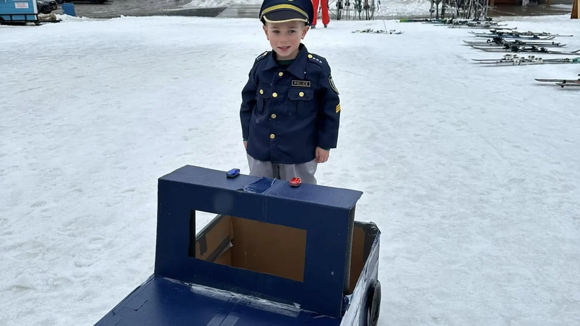 a little boy dressed as a cop standing behind his cop car sled