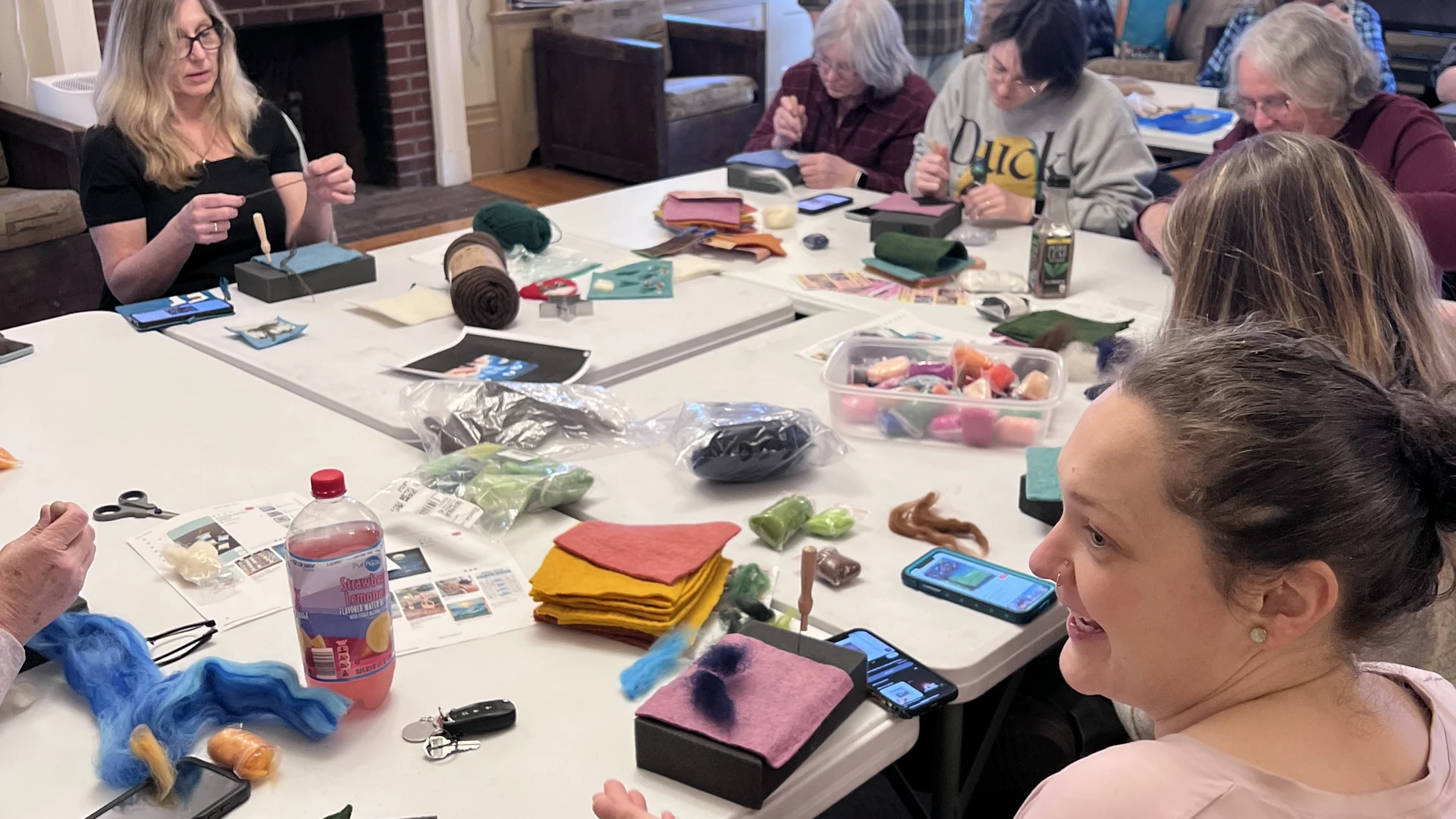 A group of people gathered around tables, working on needle felting projects.