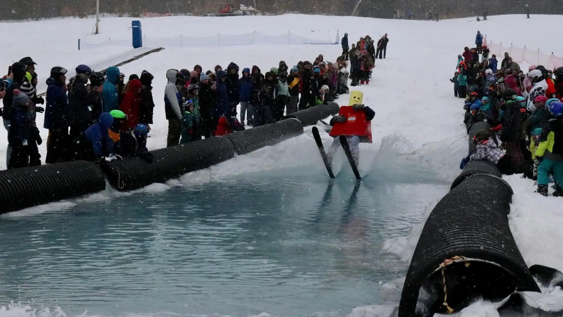 a person dressed as a LEGO mas just hitting the waters edge after skiing down the hill