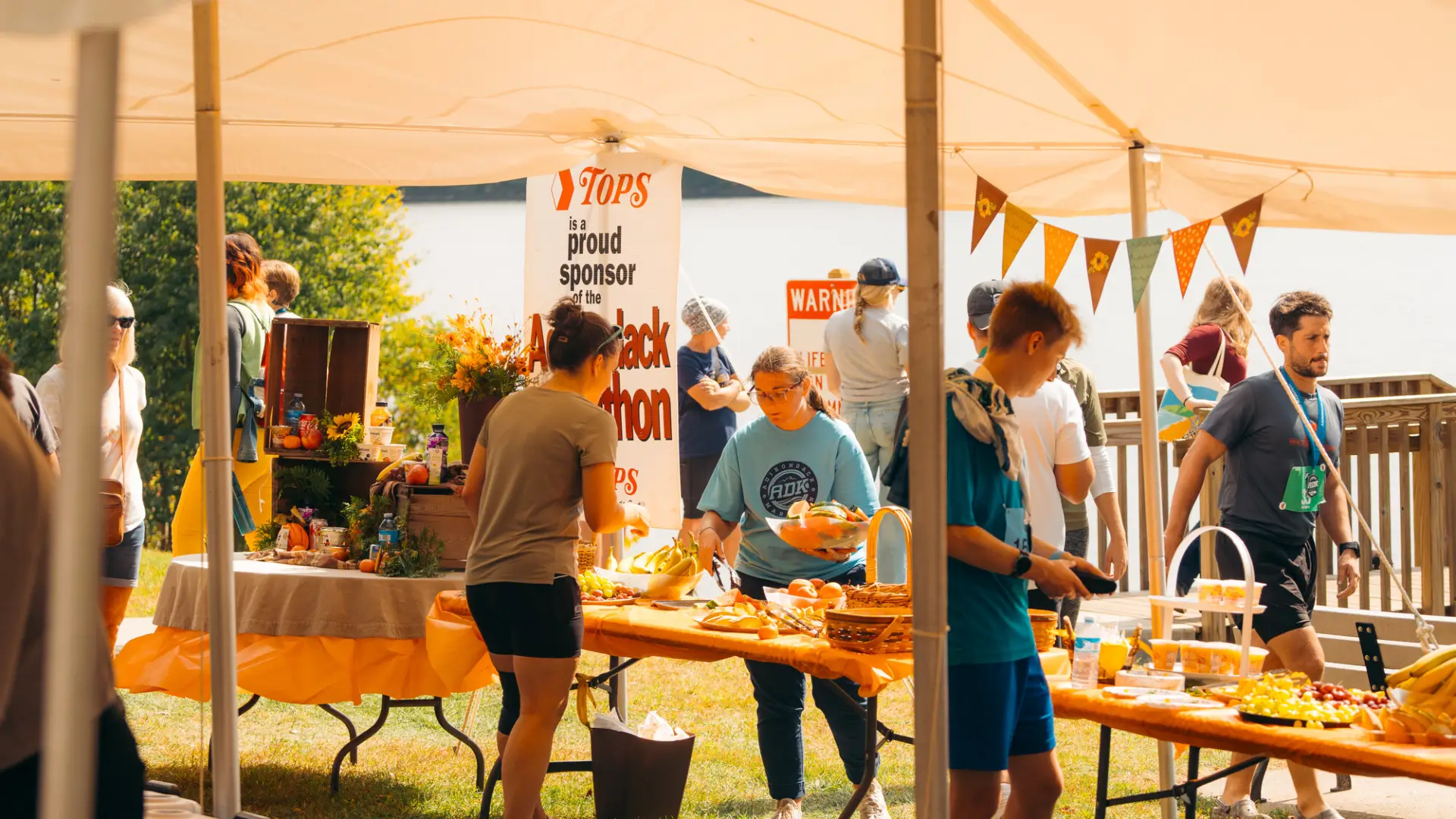 Under a tent, volunteers and participants gather around tables with fruit and snacks at the Adirondack Marathon.