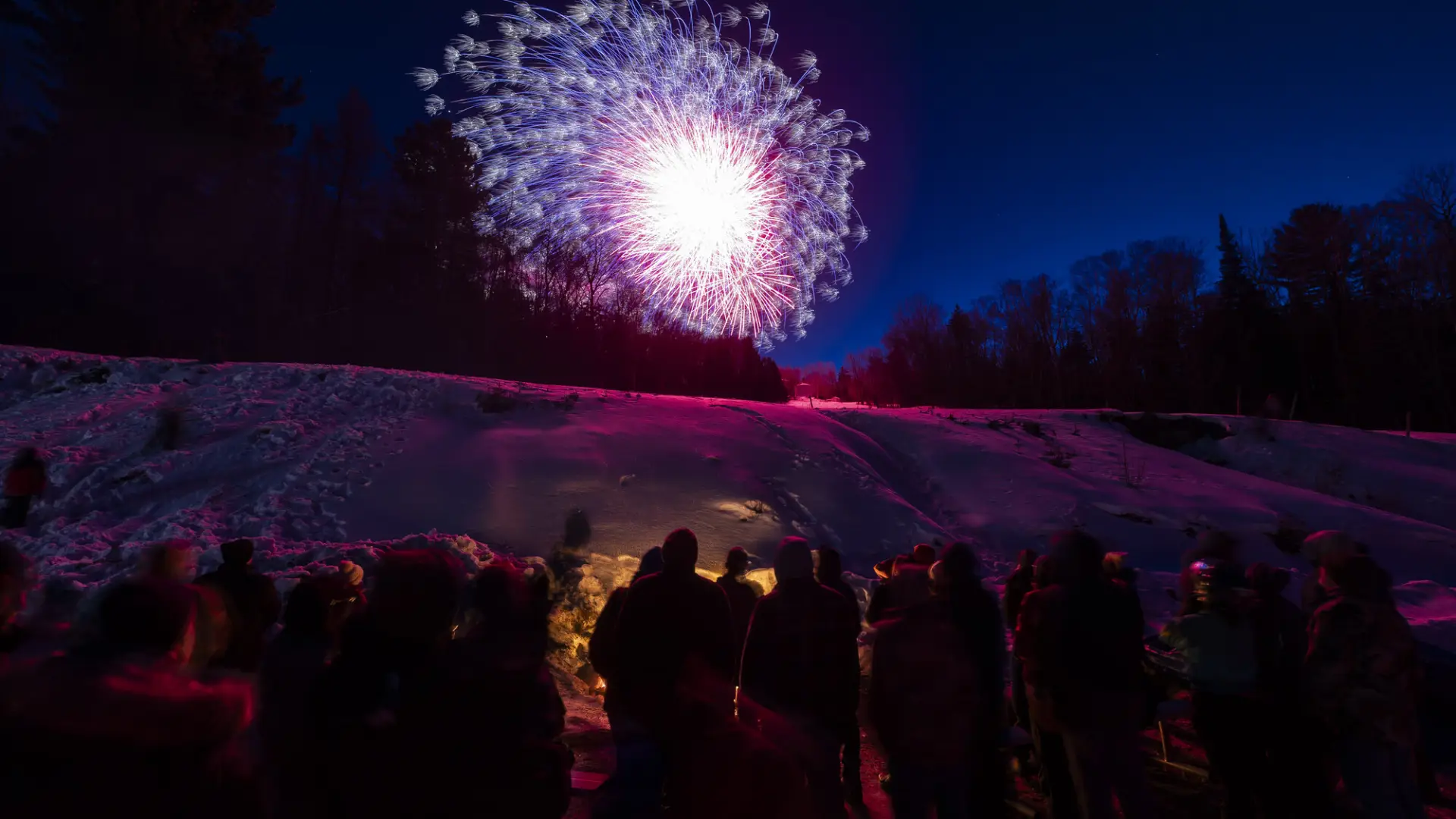 fireworks above a group of people around a bon fire