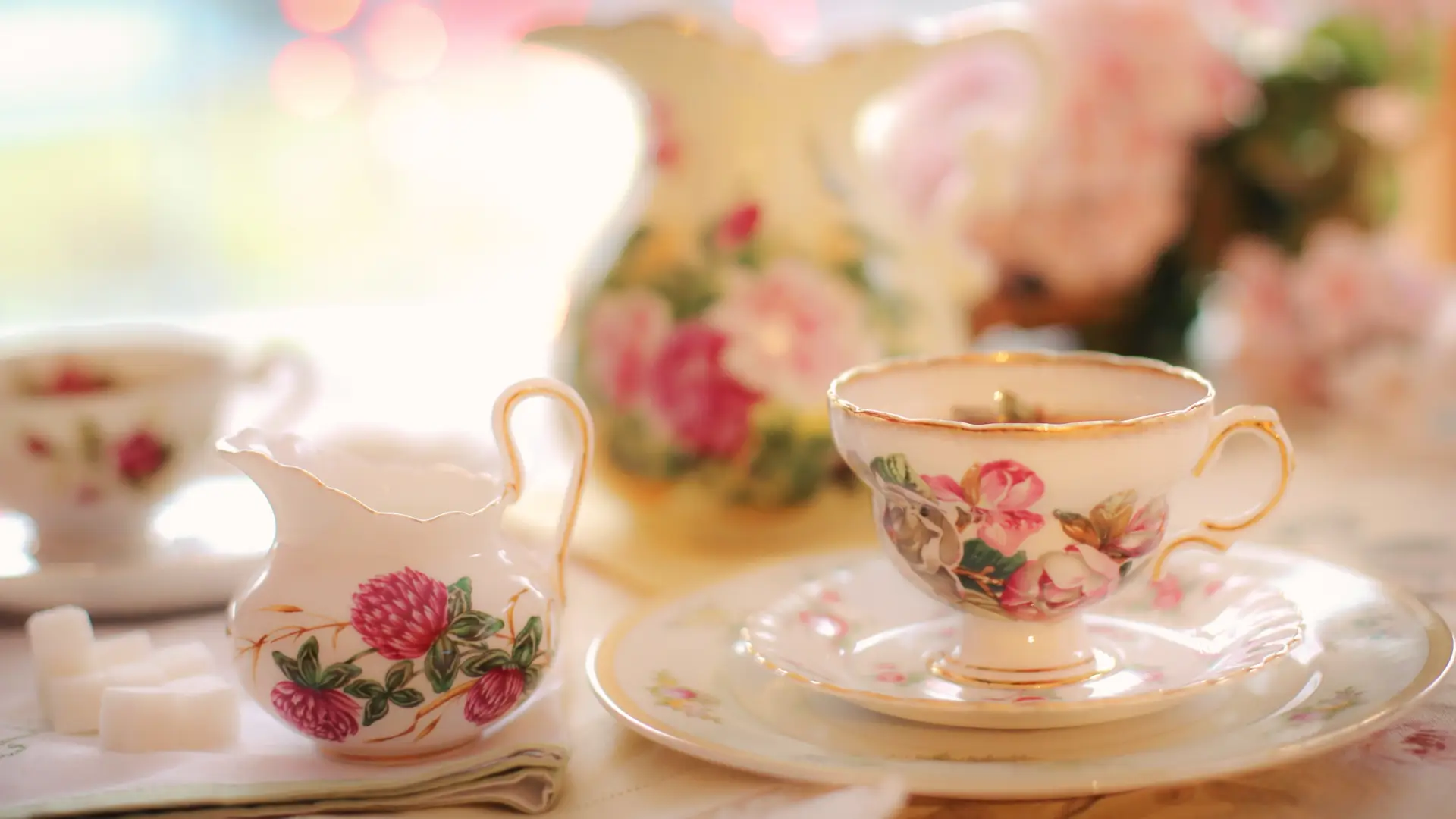 A porcelain tea set with a dark pink rose motif sits on linen table cloth covered surface