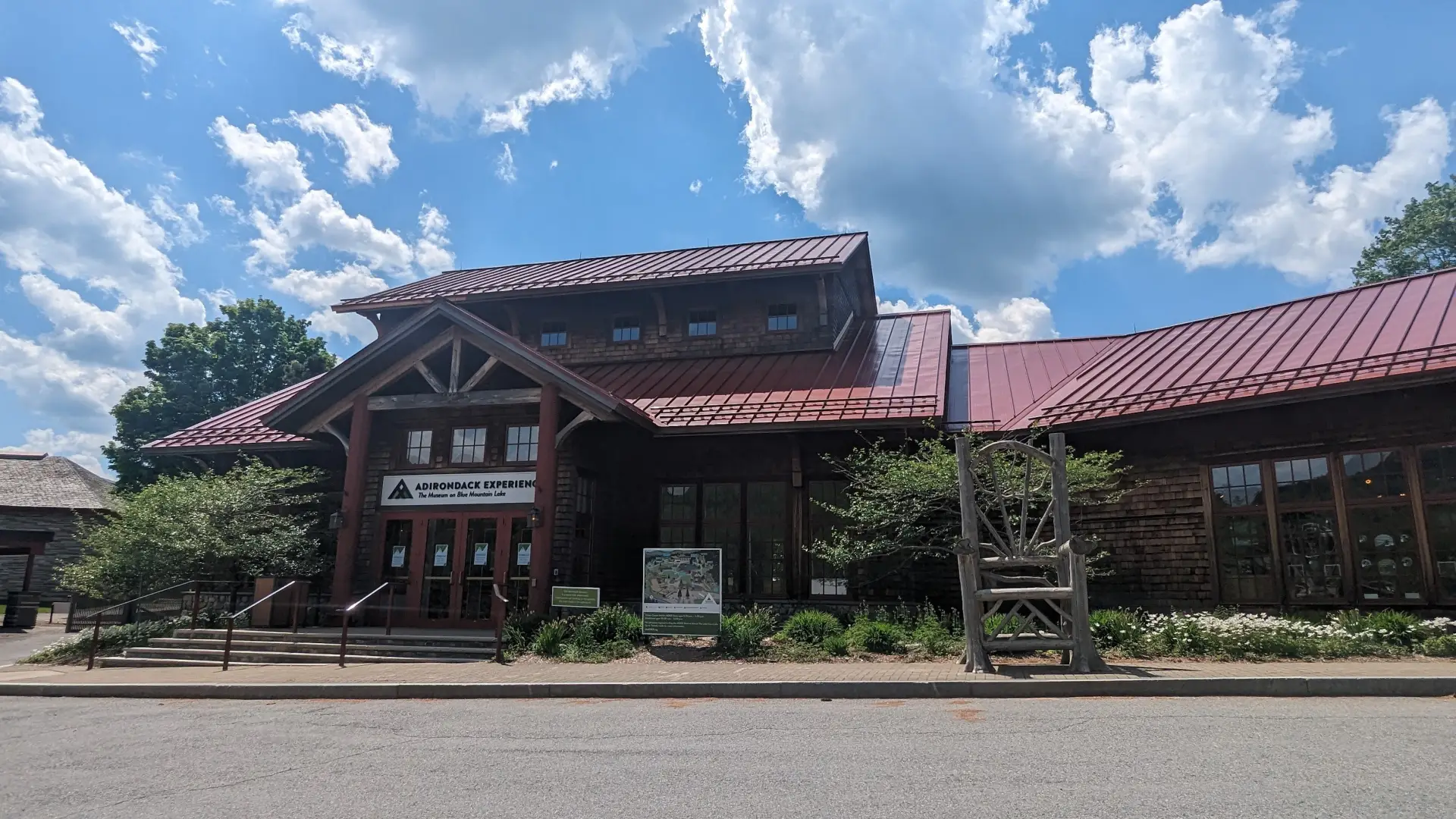 An entryway to the museum with stairs, a large sign with the name and a massive wooden chair by the sidewalk