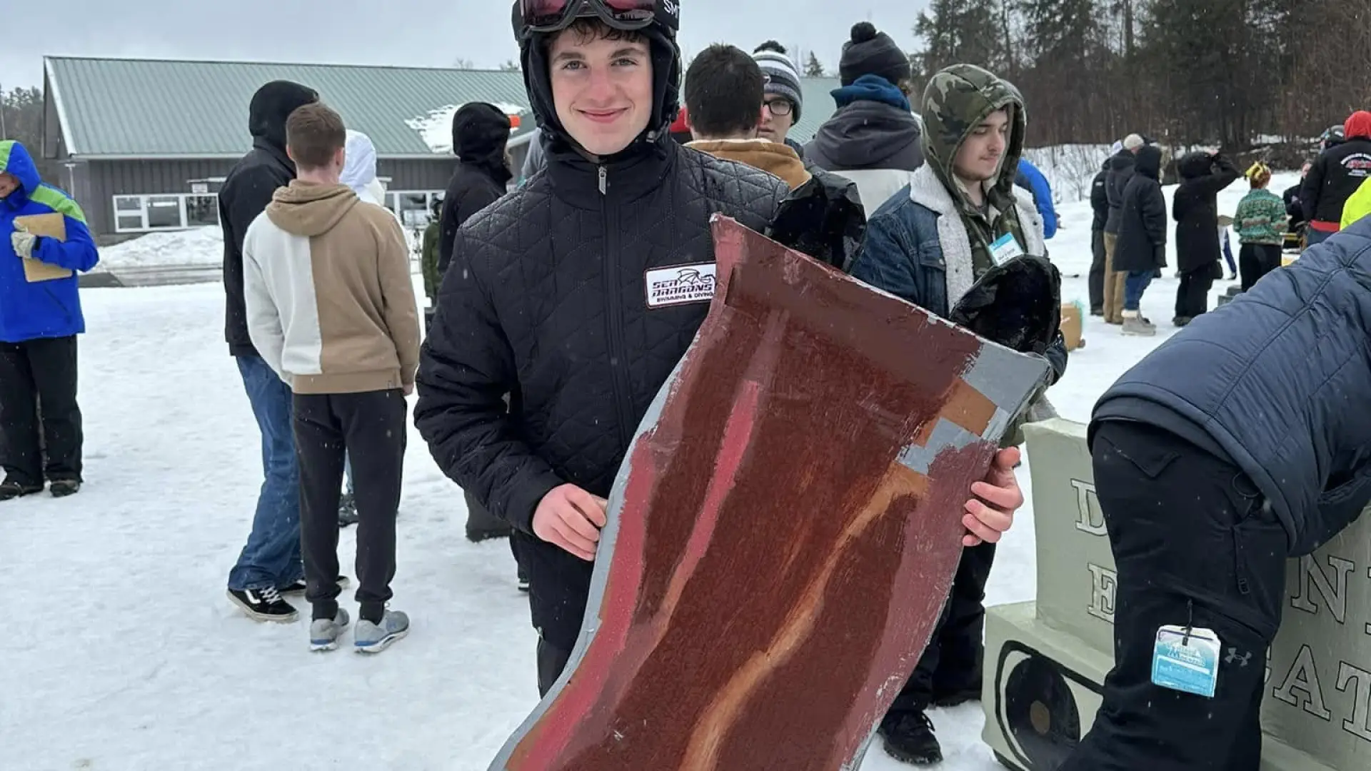 a boy holding up a sled that looks like a piece of bacon