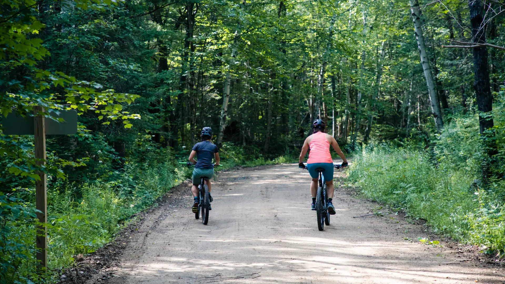 Two cyclists bike down a dirt road