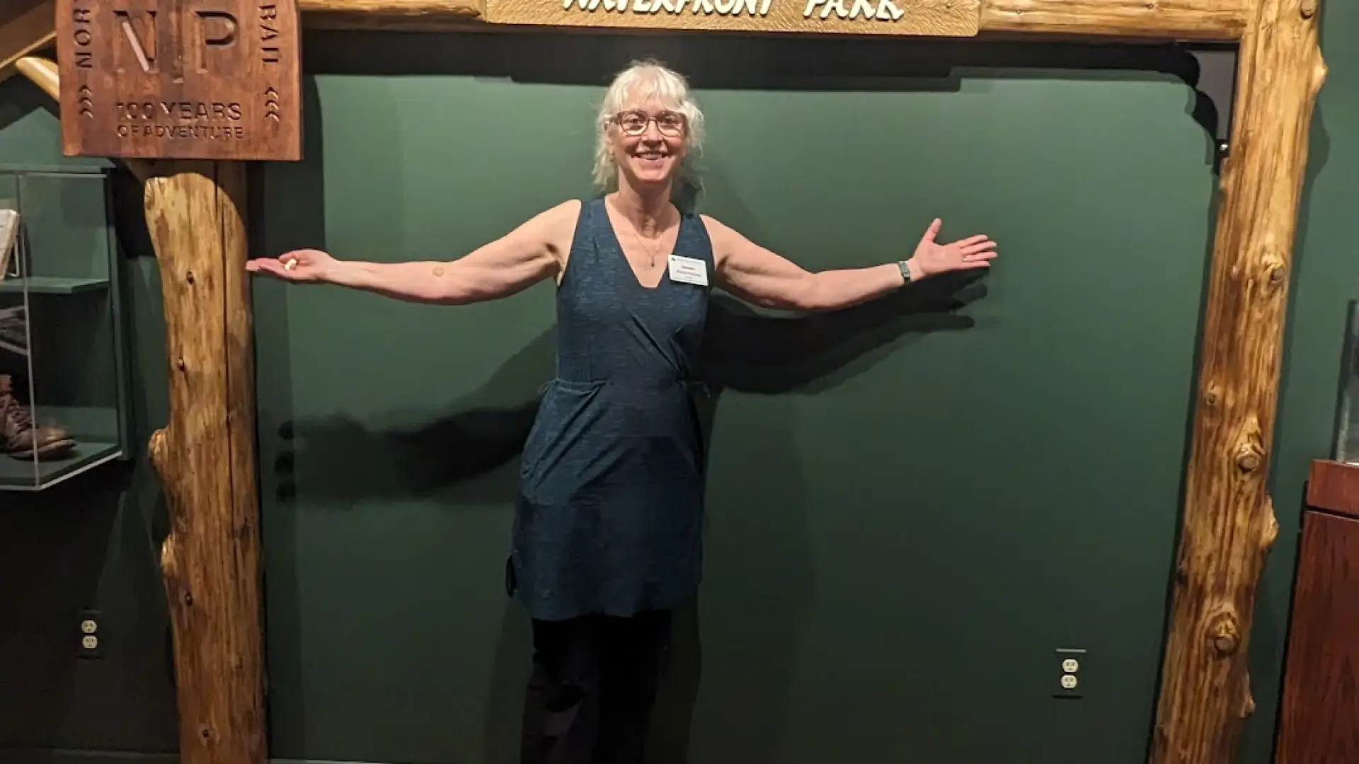 A woman smiles under a wooden arch against a green wall where plaques describing the NPT are displayed