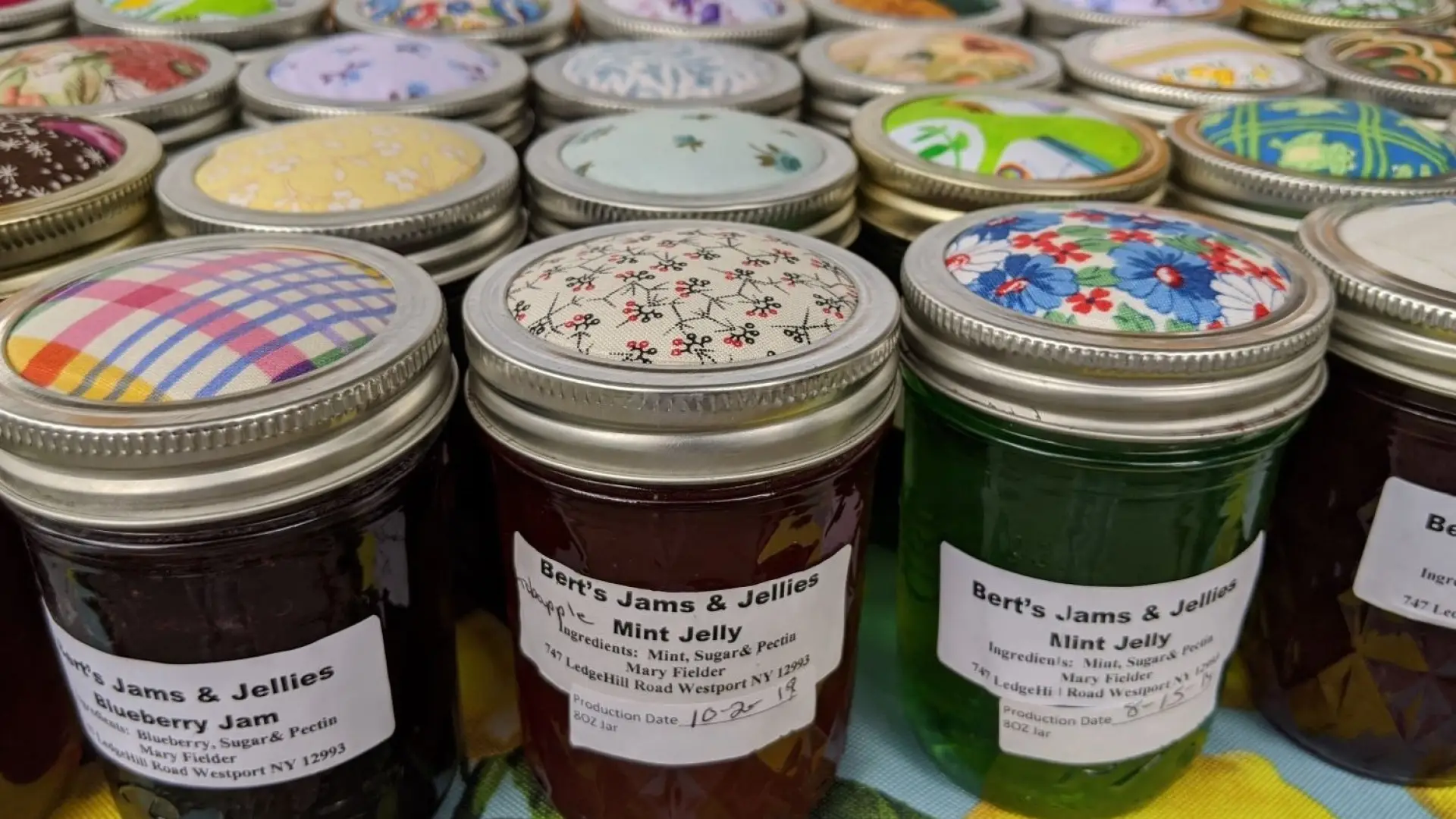 Many jars of jam sitting in clean lines with colorful fabric covering the lids