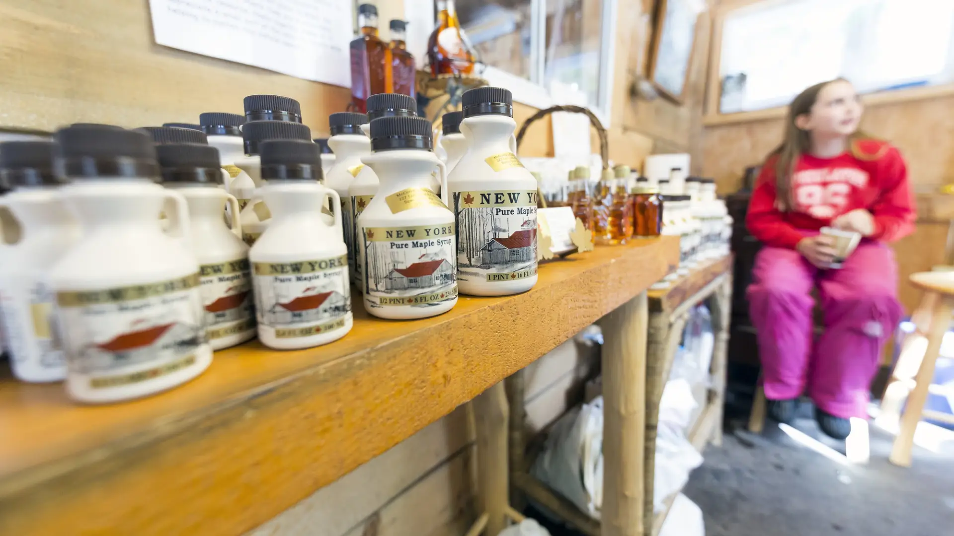 Girl sitting at the end of a table with many maple syrup bottles for sale