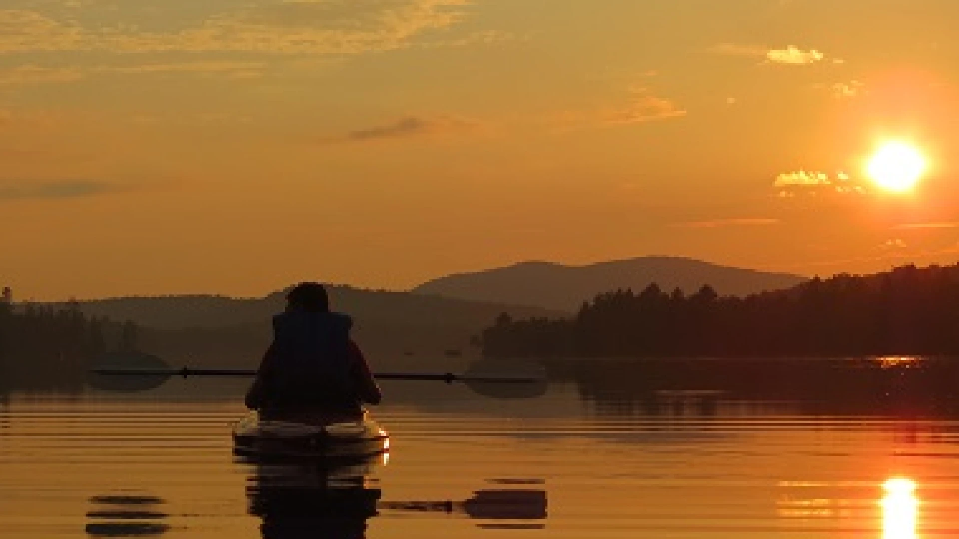 A person paddling on Lake Durant while the sunset paints the mountain sky orange.