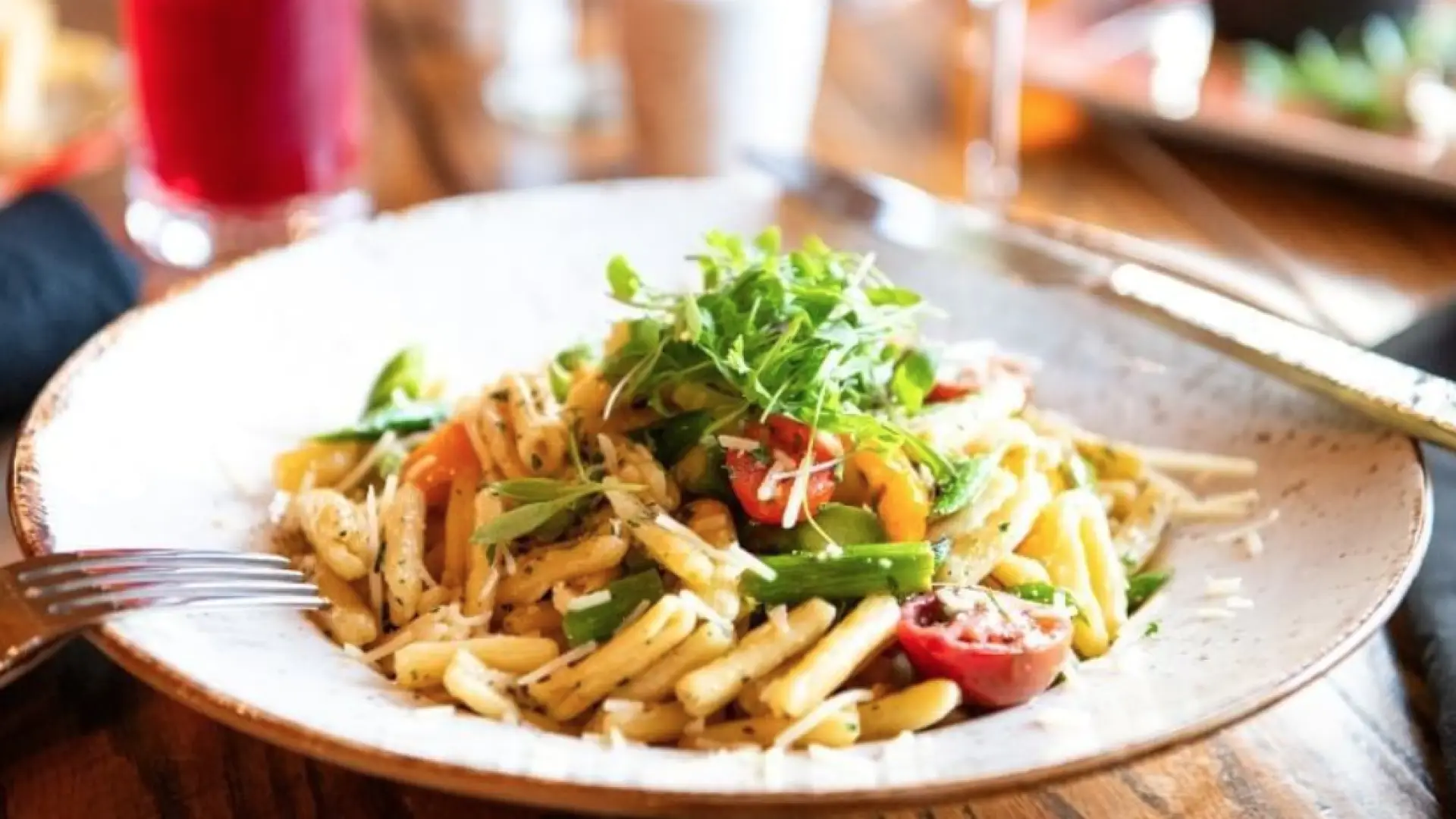 A pasta dish with cherry tomatoes, shredded parmesan and topped with microgreens.