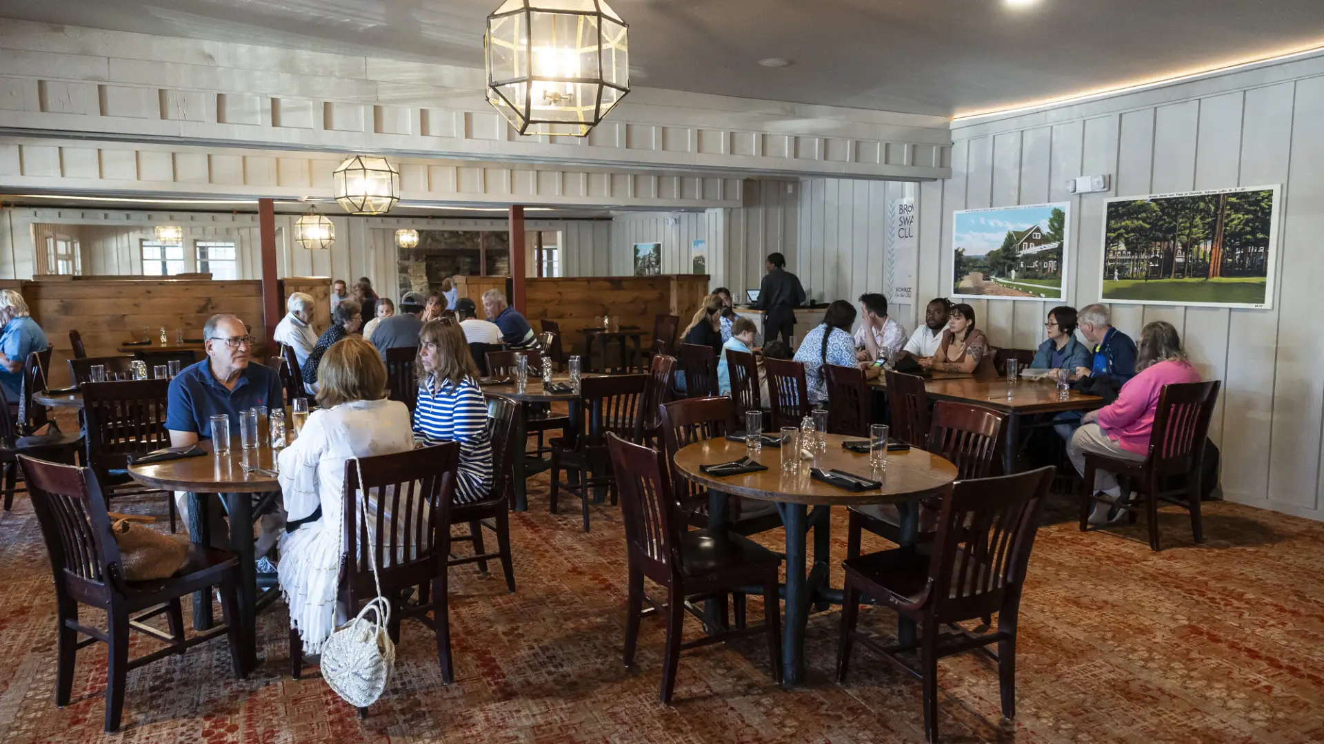 A grand dining room with chandeliers and white paneled walls filled with large wooden dining tables.
