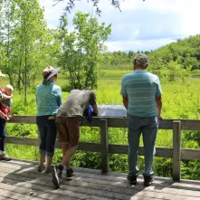 A group of people at a deck with interpretive signage on a trail