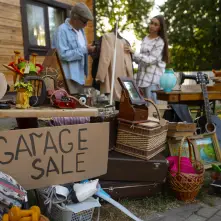 A variety of items sit outside with a hand written sign on cardboard reading Garage Sale