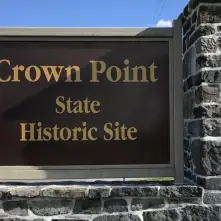 A large brown sign on a stacked stone post reading Crown Point Historic Site in gold letters