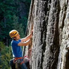 A man in a helmet, harness and ropes climbs a steep rock face.