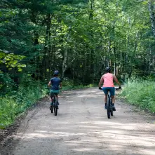 Two cyclists bike down a dirt road