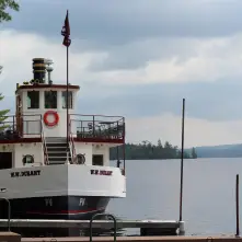 The WW Durant docked by a lush grass park with the mountains and clouds behind.