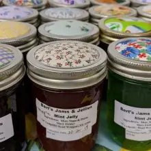 Many jars of jam sitting in clean lines with colorful fabric covering the lids