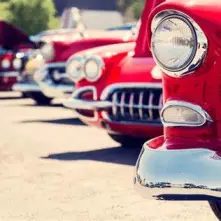 A row of classic red cars parked outdoors.
