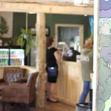 A view of the mural on the wall depicting a moose, bear and other wilderness scene with a set of leather chairs in a cozy corner, the drink fridge and people lined up to get their order in.