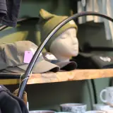 Hats adorn a mannequin head on a rough sawn shelf surrounded by other attire.