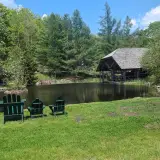 A small pond surrounded with grasses, some Adirondack style chairs for adults and kids, and two large gazebos