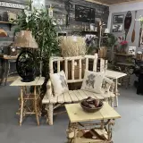 A room full of rustic decor pieces like birch wood bench and matching table and wrought iron lamps and wall hangings