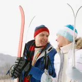 A man and woman holding skis smile at eachother