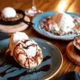 A variety of cakes, cookies, and ice creams drizzled with chocolate.