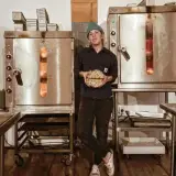 owner/baker in front of ovens