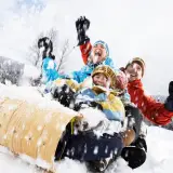 A young family laughs their way down the sledding hill on a tobogan as the snow flies around them