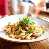 A pasta dish with cherry tomatoes, shredded parmesan and topped with microgreens.