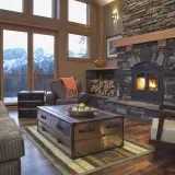 The main living space of a large home with two stories of windows, a stone fireplace with built in wood storage and ample lush seating.