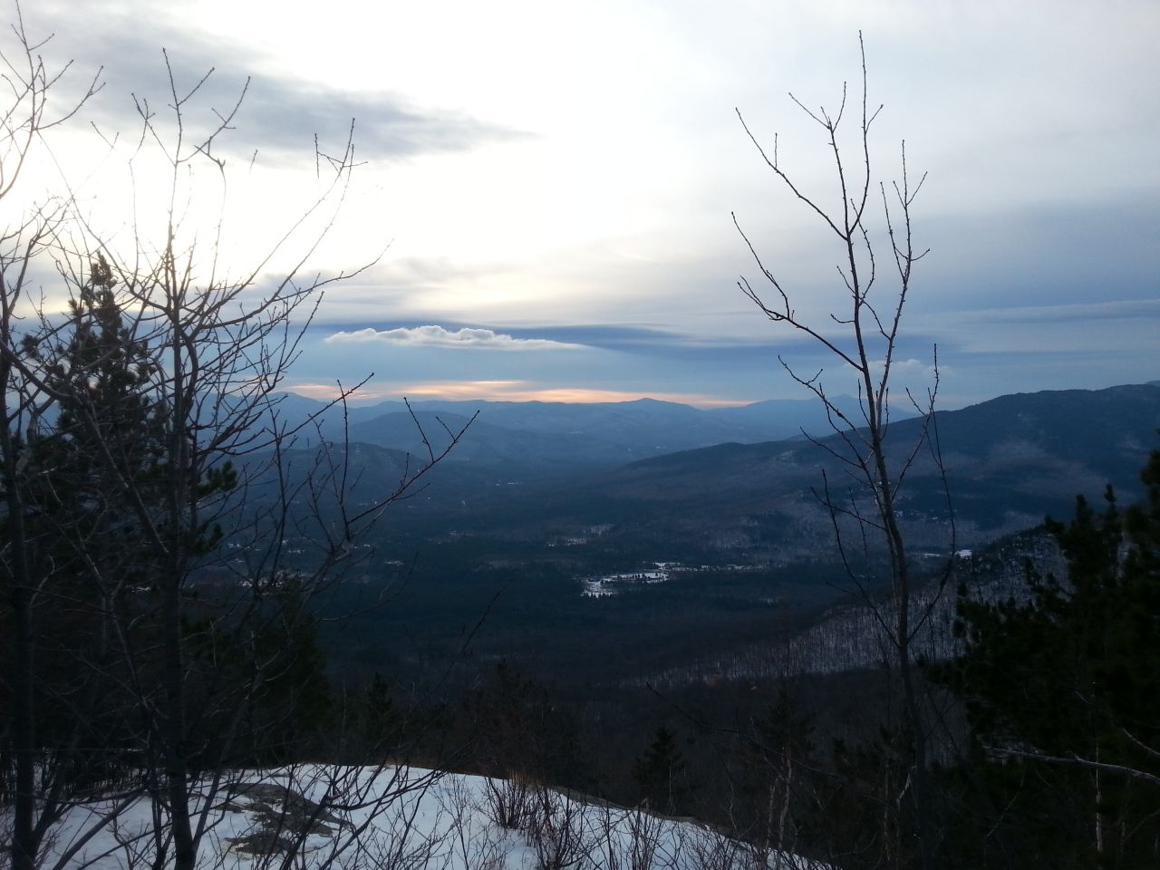 A view from a mountain top in winter overlooking a dark mountain range.