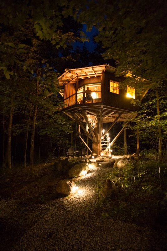 A man stands at the top of a treehouse at night.