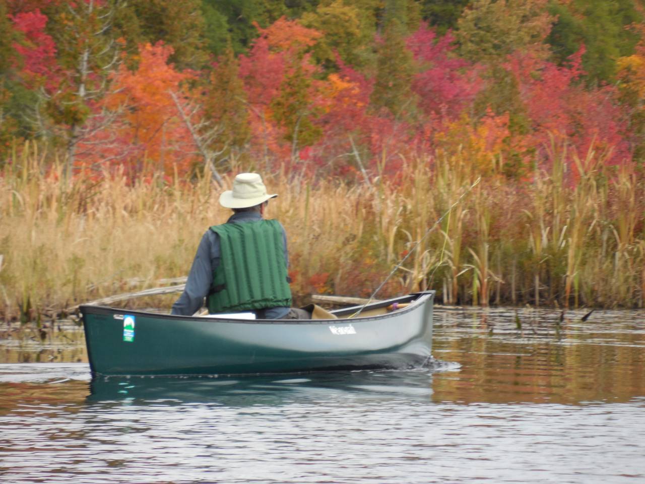 A person canoeing and fishing in the fall.